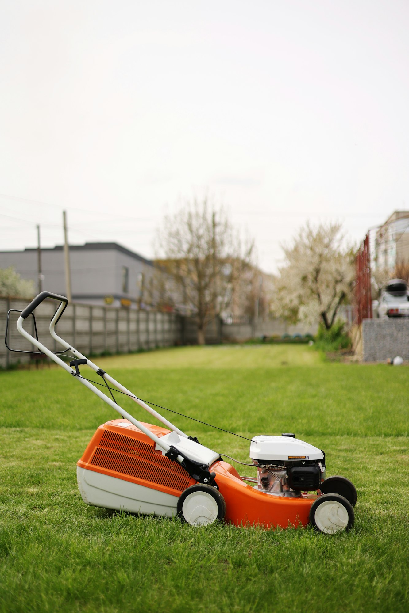 Modern orange-grey electric lawn mower on bright lush green lawn at residential backyard of house. G